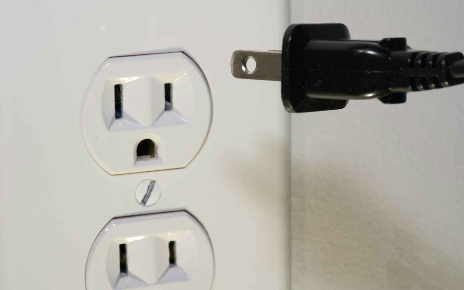 A black power plug held just short of a white wall socket