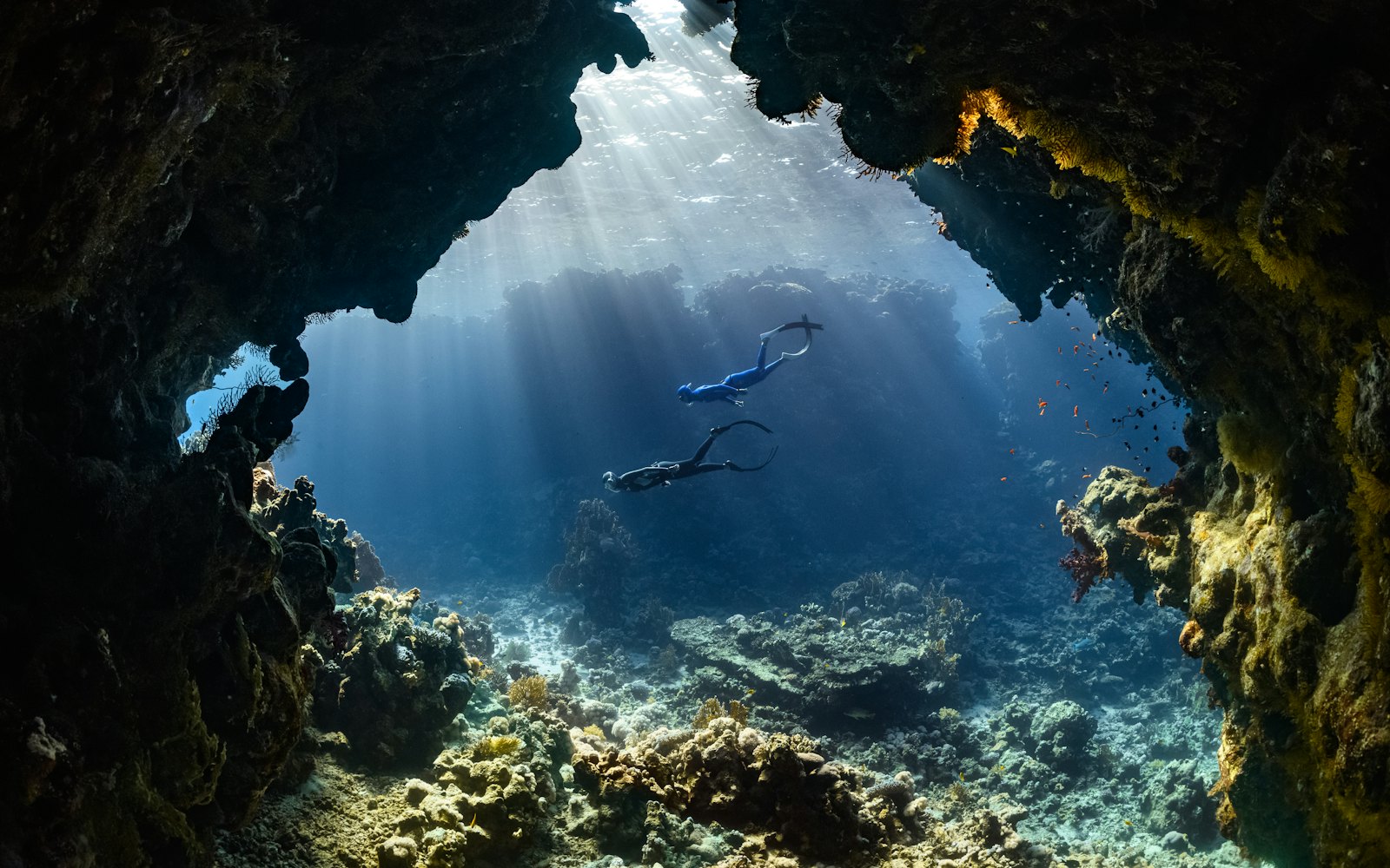Two divers swimming through an underwater cave toward the light