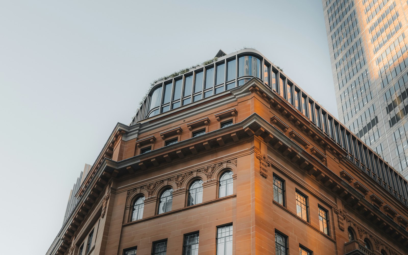An old sandstone building with a modern glass tower behind it
